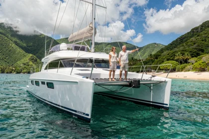 Couple sur un catamaran blanc ancré dans une baie turquoise en Martinique avec collines verdoyantes en arrière-plan